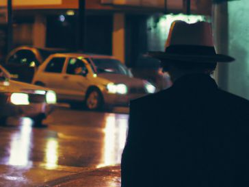 La lluvia cae en la ciudad, mojando los edificios altos y las calles llenas de gente apresurada. En una esquina, un hombre con sombrero y gabardina espera pacientemente a su contacto. ¿Qué secreto oscuro están intercambiando?
